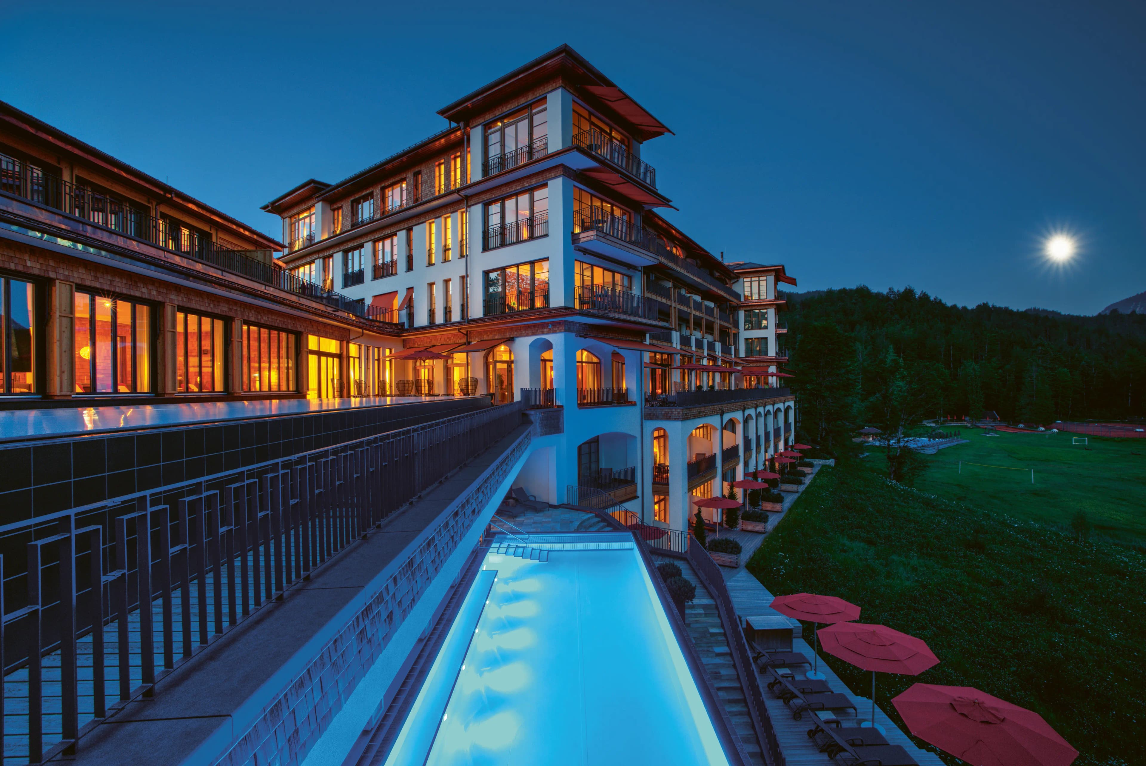 Schloss Elmau Retreat bei Dämmerung — Fassade mit beleuchtetem Außenpool (Foto: © Schloss Elmau)